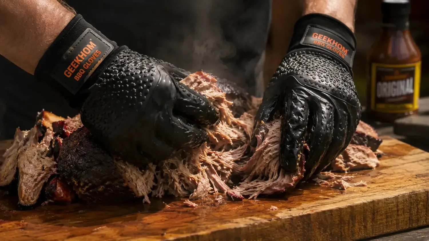 Woman using silicone BBQ gloves to pull apart a smoked pork shoulder into shreds on a cutting board