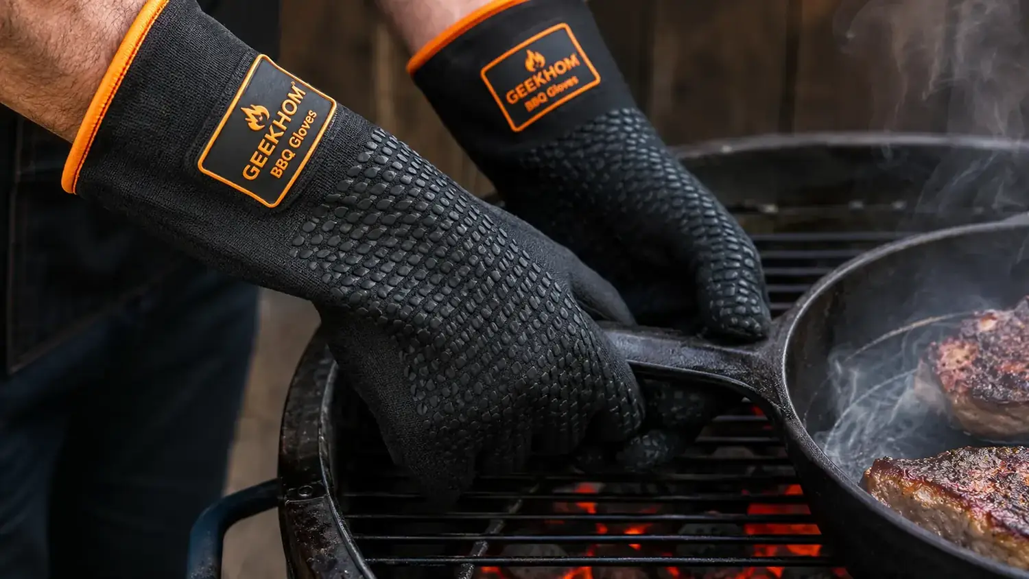 Close-up of GEEKHOM silicone BBQ gloves being used to move a cast-iron skillet on a hot charcoal grill