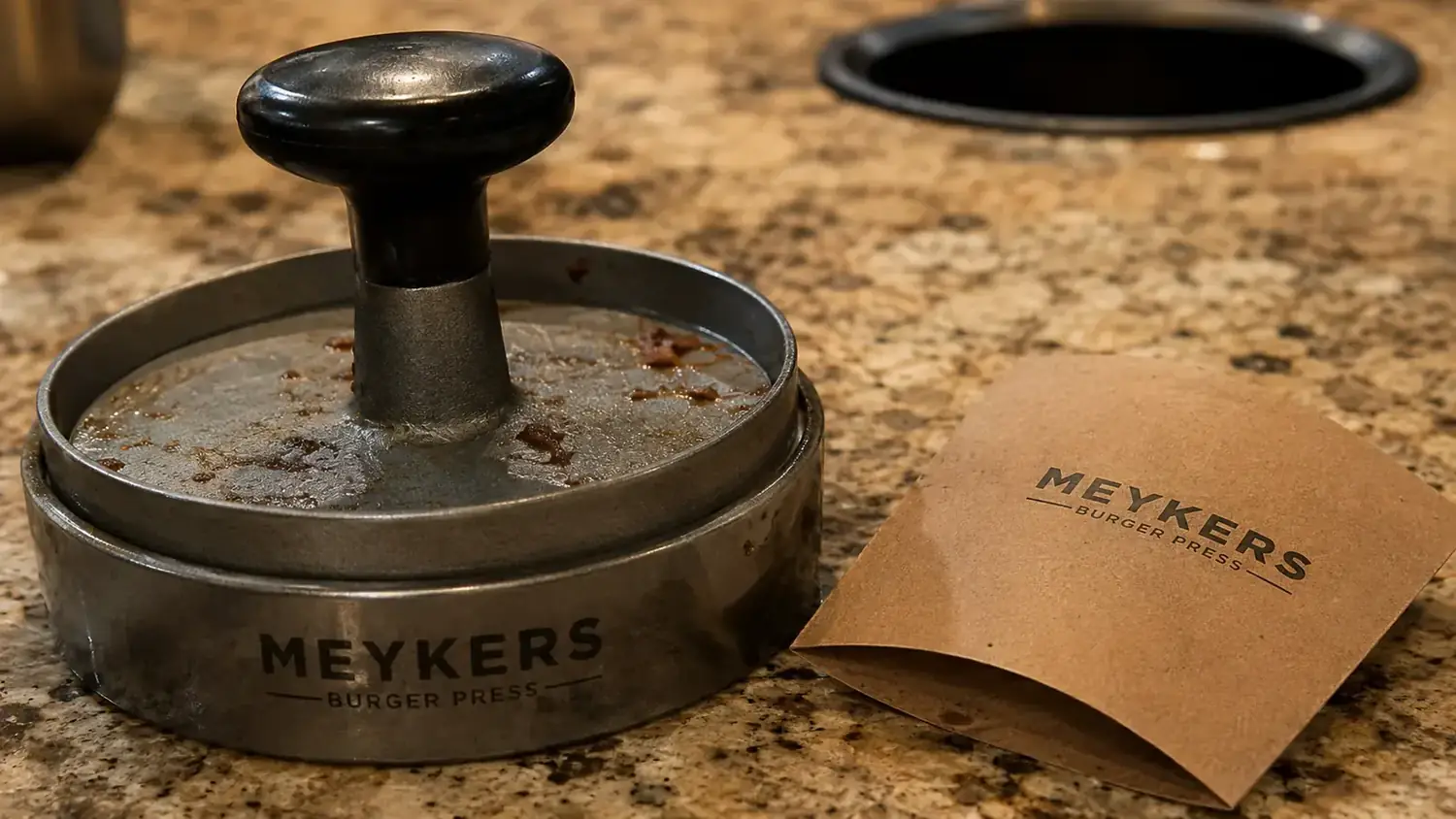 Empty box of Meykers patty papers sitting next to a burger press with no papers left and a burger patty stuck to the surface