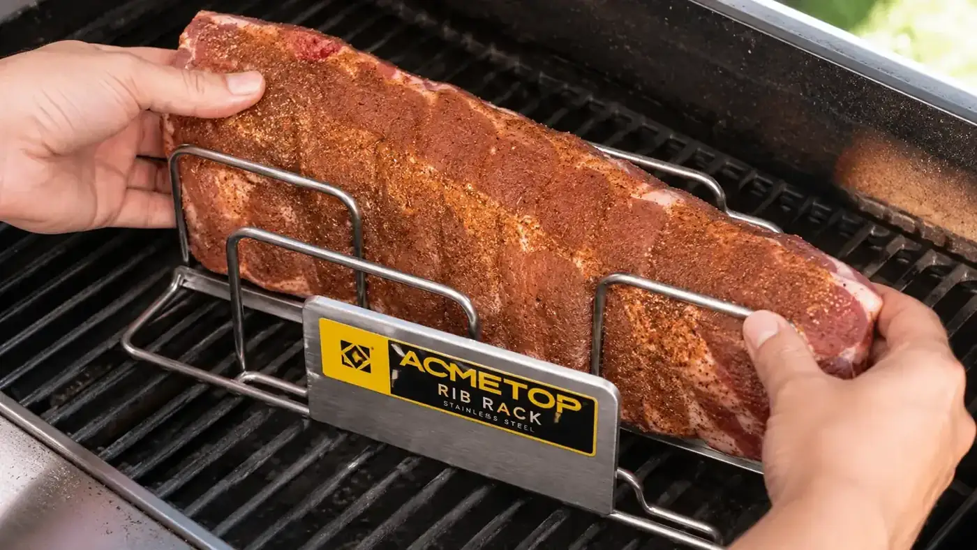 Hands placing a rack of baby back ribs into the slots of a stainless steel rib rack on a gas grill grate